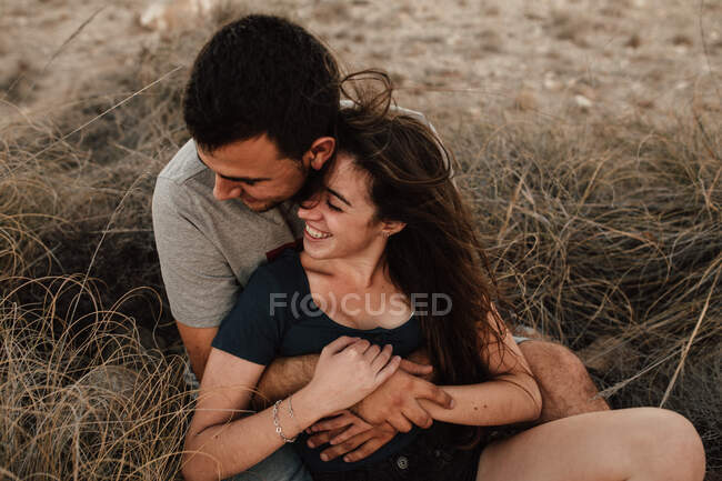 Retrato de novio feliz y novia abrazándose sobre hierba seca en el campo - foto de stock