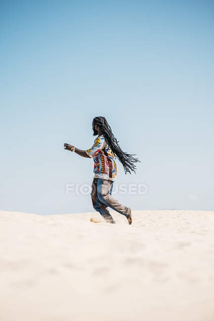 Man with dreadlocks walking on desert — Stock Photo