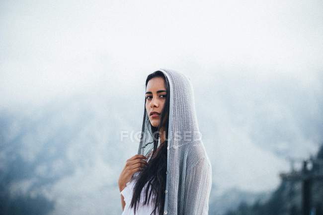 Чувственная женщина в меченой толстовке, позирующая над туманным горным ландшафтом — стоковое фото