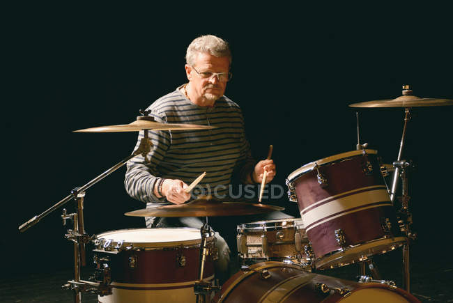 Mature man playing drums against black — Stock Photo