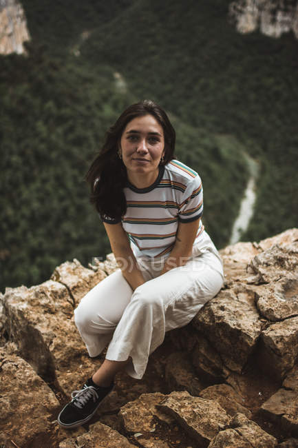 Brunette femme assise sur la pierre et regardant la caméra — Photo de stock