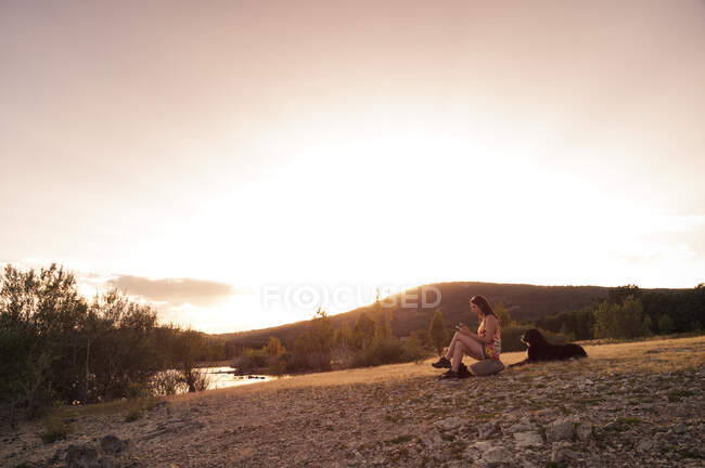 Молода жінка зі своєю собакою насолоджується розслабленим під час заходу сонця — стокове фото