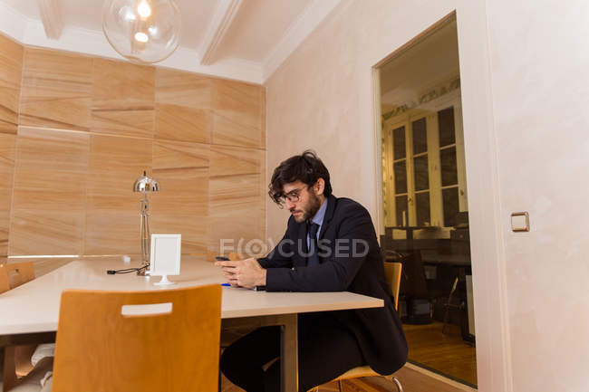 Mann im schwarzen Anzug sitzt im Besprechungsraum und schreibt SMS auf Smartphone. — Stockfoto