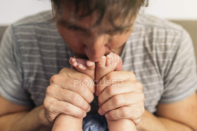Primer plano del padre adulto besando tiernamente los pies de su bebé - foto de stock