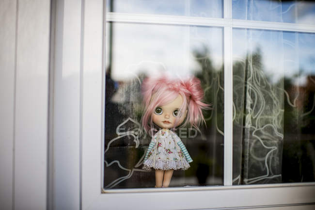 Vue rapprochée de poupée moderne aux cheveux roses debout derrière la fenêtre — Photo de stock