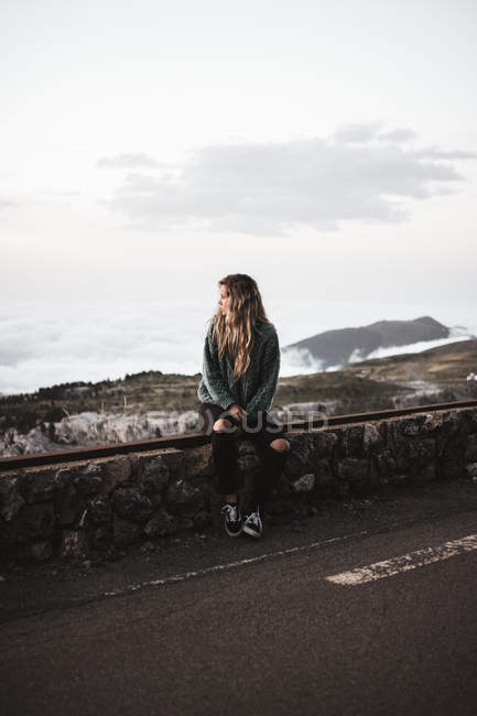 Femme assise au bord de la route et regardant le paysage — Photo de stock