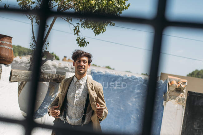 Portrait of handsome smiling man in stylish clothes looking at camera in sunlight.Fence on background. — Stock Photo