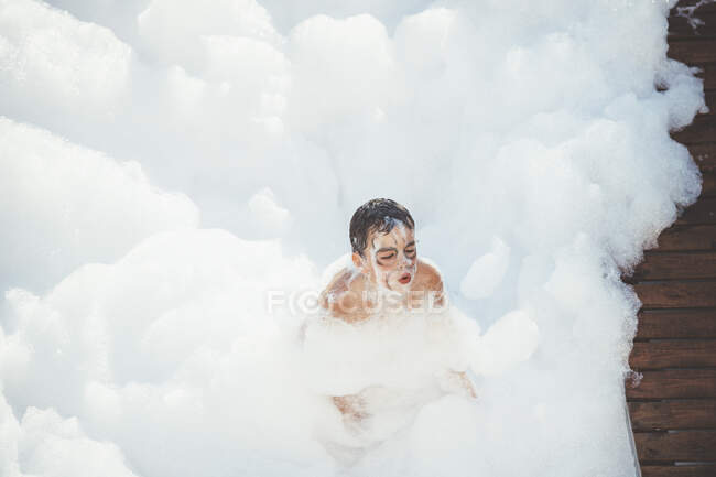 Веселый ребенок играет в белой пене — стоковое фото