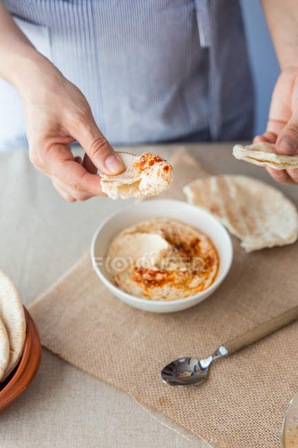 Mani immergendo il pane pita nell'hummus — Foto stock