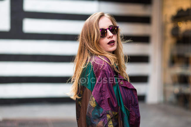 Young stylish girl in sunglasses looking aside over shoulder — Stock Photo