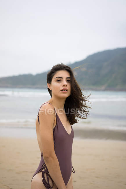 Portrait of brunette girl in swimsuit posing on beach and looking at camera — Stock Photo