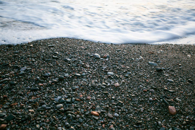 Vue grand angle de la plage de galets avec mousse de mer — Photo de stock