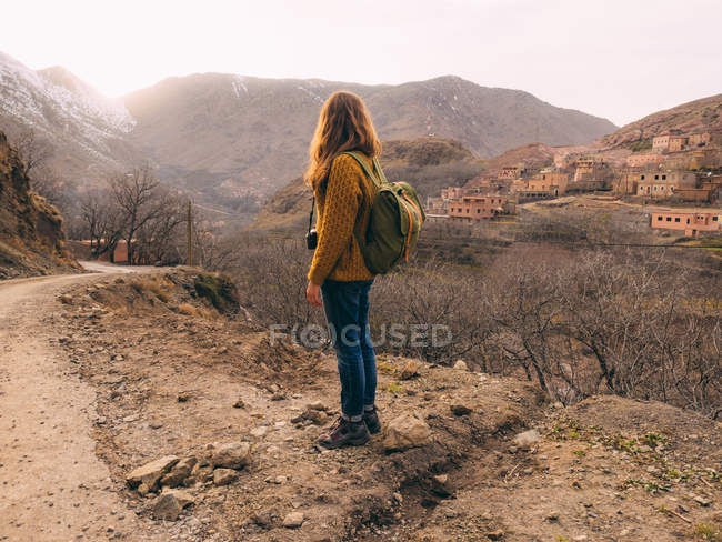 Vista lateral de turista con mochila contra ciudad en paisaje montañoso - foto de stock