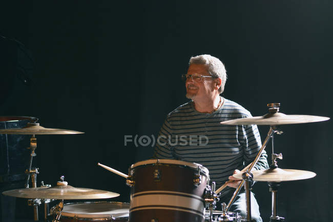Зрелый мужчина, сидящий на сцене и играющий на барабанах, улыбаясь — стоковое фото