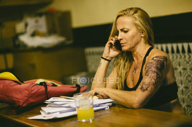 Retrato de mulher tatuada com papéis falando ao telefone no bar. — Fotografia de Stock