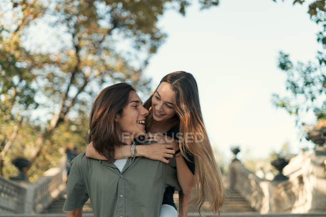 Portrait of boyfriend giving piggy back to girlfriend on stairs in park — Stock Photo