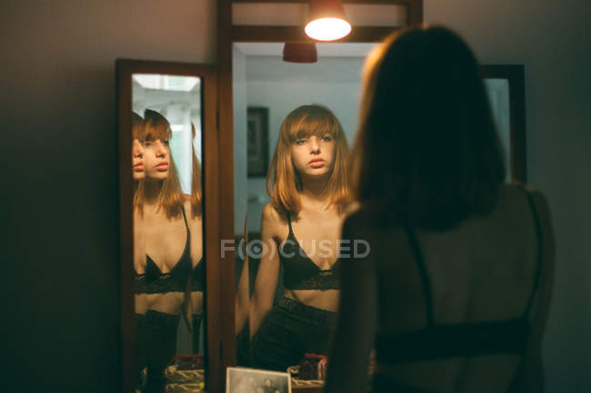 Rear view of young woman in black bra standing at mirrors — Stock Photo