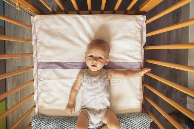 Adorable bébé regardant la caméra tout en étant couché dans la vue cot.Above. — Photo de stock