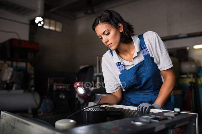 Mecânico fêmea que inspeciona o motor do compressor com lanterna elétrica — Fotografia de Stock