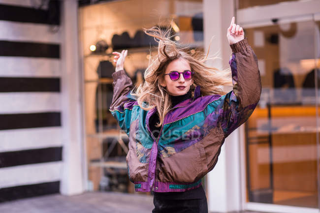 Menina elegante jovem em óculos de sol posando com os braços levantados — Fotografia de Stock
