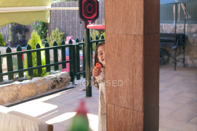 Chica feliz escondido detrás de la columna y apuntando con armas de agua - foto de stock