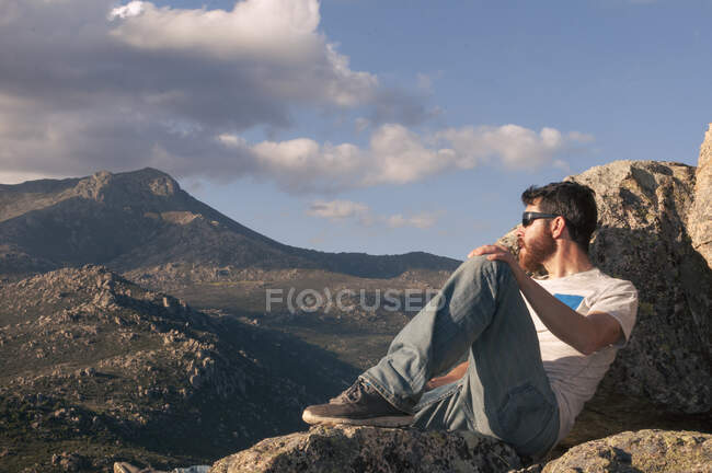 Розслаблений молодий чоловік засмагає на вершині гори на заході сонця — стокове фото