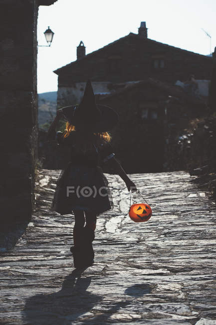 Menina em traje de bruxa andando rua pavimentada — Fotografia de Stock