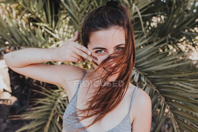 Smiling brunette woman looking at camera while doing camouflage make-up on cheek — Stock Photo
