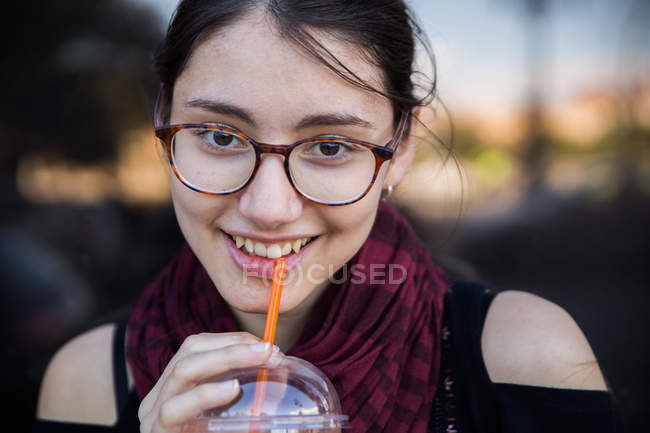 Молода жінка в окулярах п'є смузі і дивиться на камеру — стокове фото