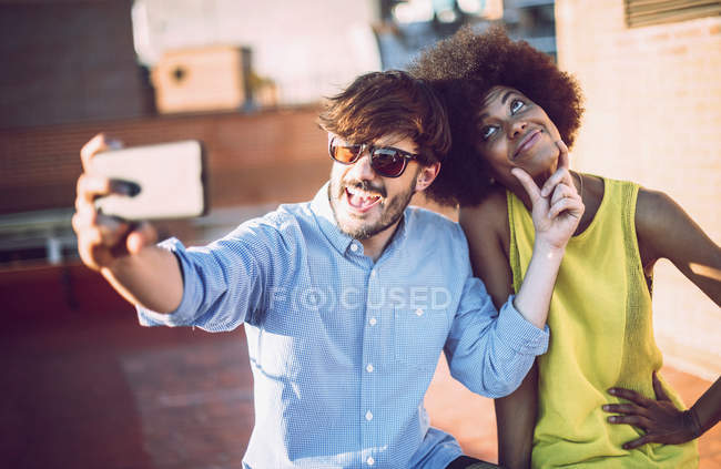 Cheerful interracial couple taking selfie on rooftop — Stock Photo