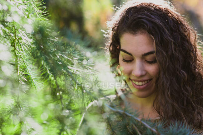 Front view of young beautiful Latina woman looking down and posing nearby conifer. — Stock Photo