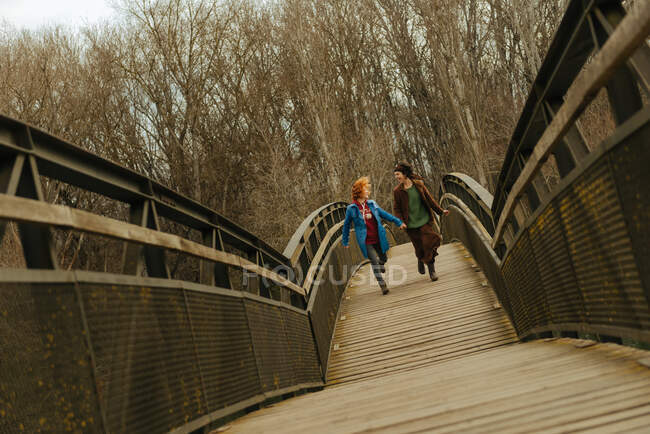 Mujeres corriendo por el puente y tomadas de la mano en el parque. - foto de stock