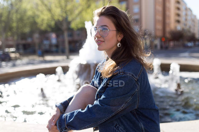 Femme en lunettes assise à la fontaine — Photo de stock