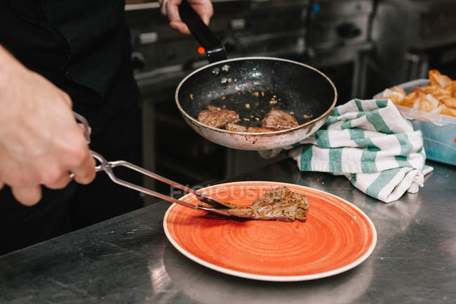 Seção média de cozinhar colocando ingredientes com pinças em pratos na cozinha do restaurante — Fotografia de Stock