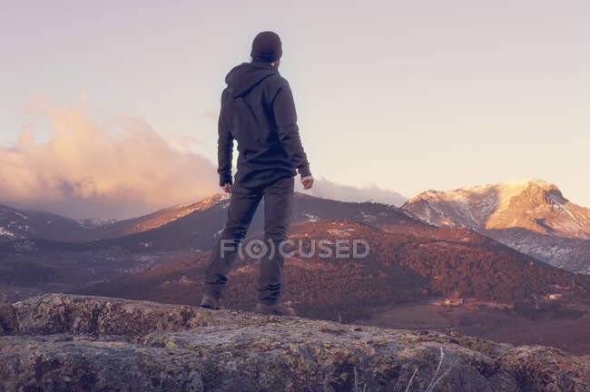 Mann auf dem Gipfel des Berges steht auf dem Felsen und beobachtet einen schönen Sonnenaufgang im sonnigen, schneebedeckten Berg — Stockfoto