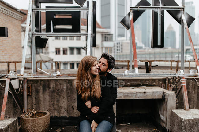 Lovely couple sitting on rooftop with great city view on background. — Stock Photo