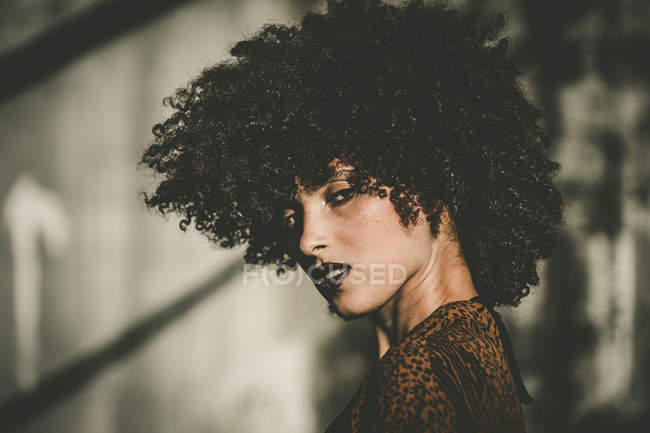 Chica expresiva con corte de pelo afro mirando por encima del hombro a la cámara - foto de stock