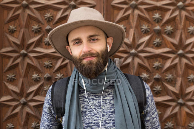 Bearded man listening to music and looking at camera over ornate wooden door. — Stock Photo