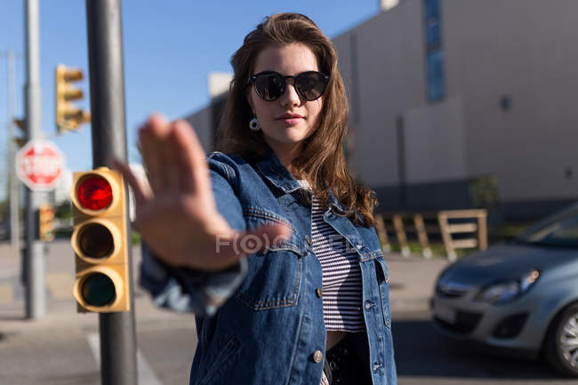 Красивая женщина в солнечных очках стоит на светофоре и жестикулирует стоп — стоковое фото