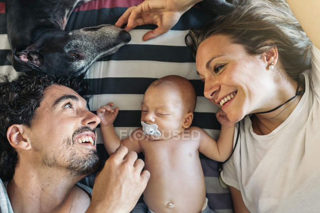 Jovem casal feliz deitado com seu bebê recém-nascido — Fotografia de Stock