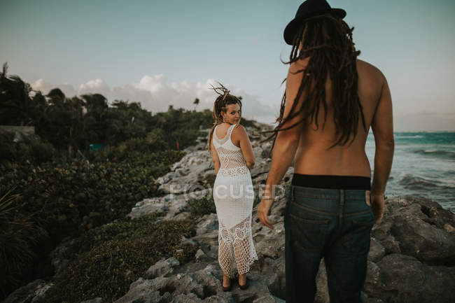 Женщина смотрит через плечо на мужчину, стоящего спиной к каменистой тропической береговой линии — стоковое фото