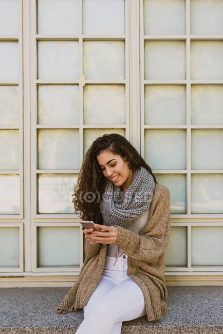 Retrato de uma menina bonita com cabelo ondulado usando seu smartphone — Fotografia de Stock