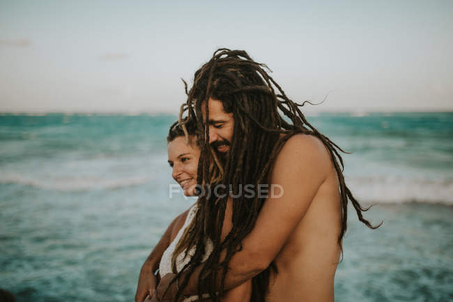 Side view of couple with dreadlocks embracing on ocean coast — Stock Photo