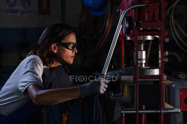 Side view of female mechanic in protective googles operating hydraulic press — Stock Photo