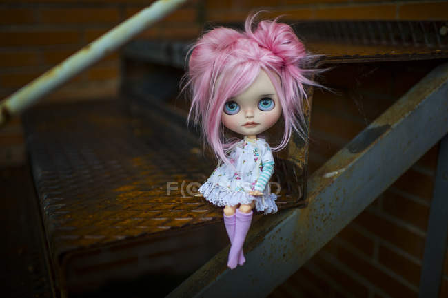 Vista de cerca de la muñeca moderna de pelo rosa sentada en las escaleras - foto de stock