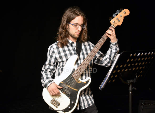 Junger Mann spielt Bassgitarre gegen Schwarz — Stockfoto