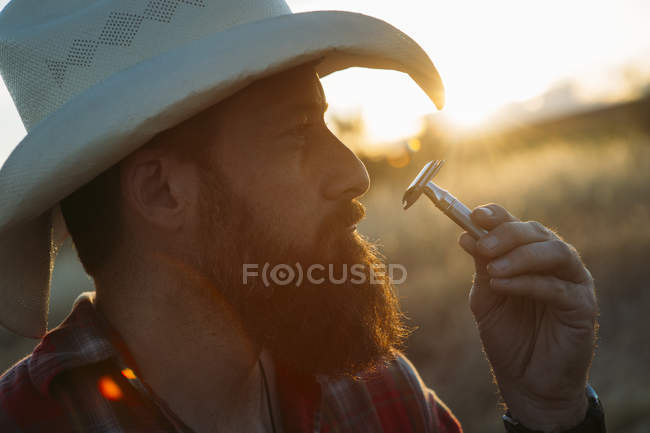 Portrait of bearded man in cowboy hat posing with vintage double-edge razor — Stock Photo