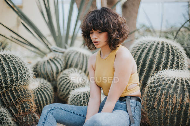 Brunette girl sitting by cacti and looking down — Stock Photo