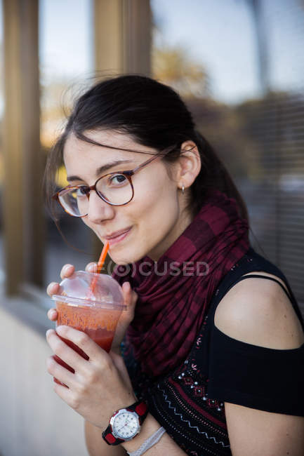 Junge brünette Frau trinkt Smoothie und schaut in die Kamera — Stockfoto