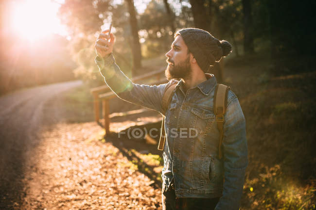 Side view of man doing self-shooting on autumn road in woods. — Stock Photo